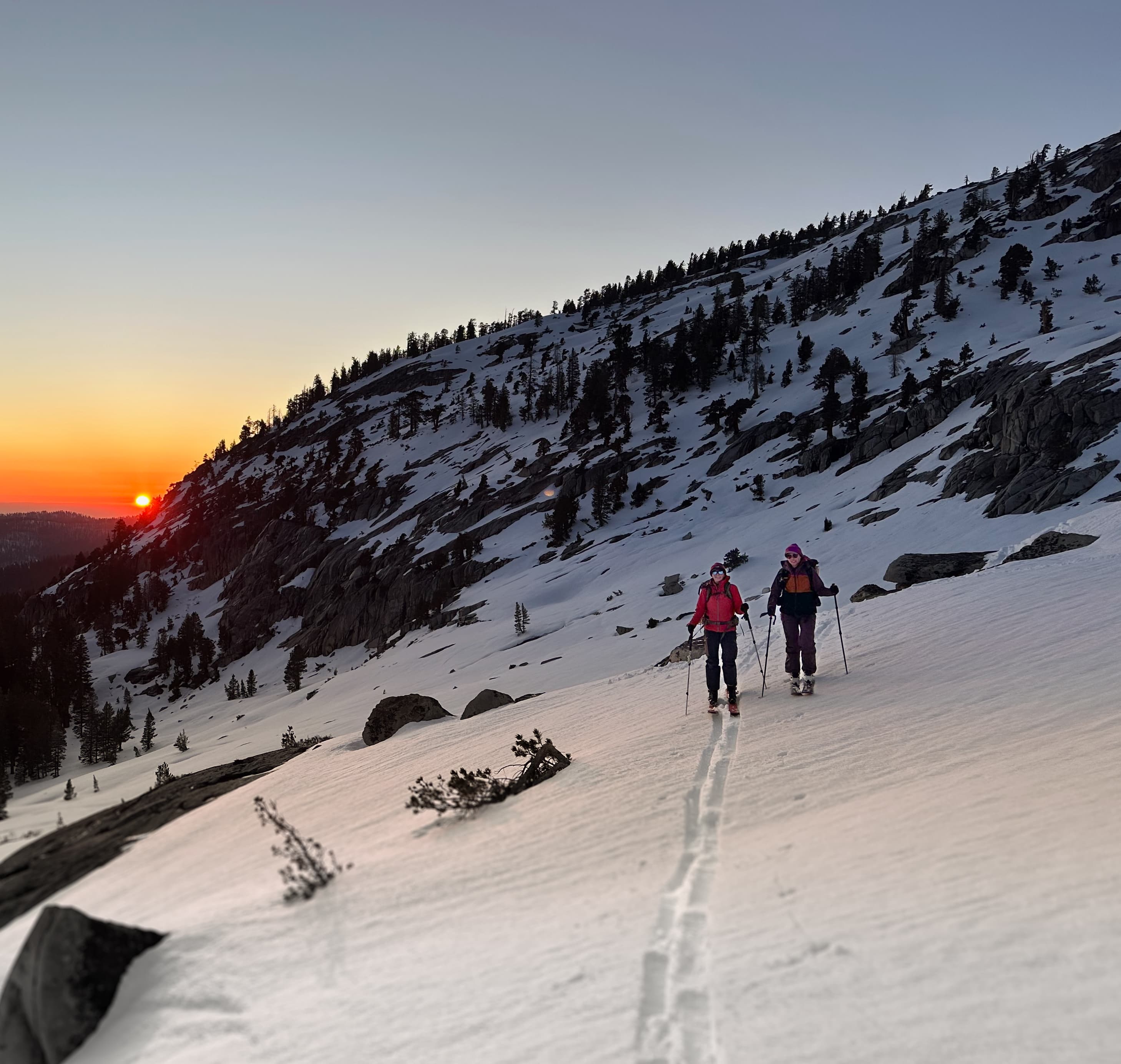 Two skiers skinning up a steep alpine slope at sunset